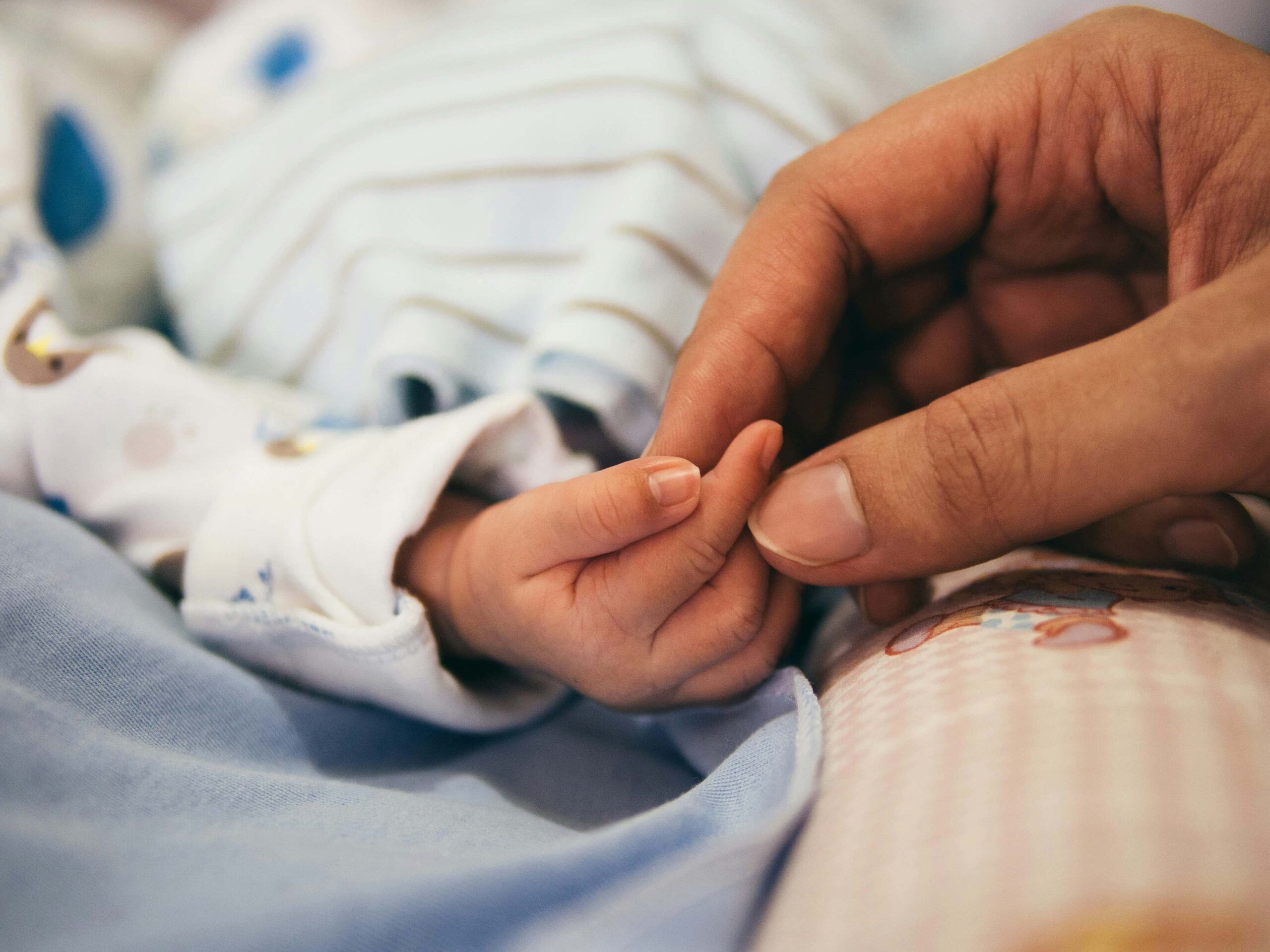 newborn baby and parent holding hands